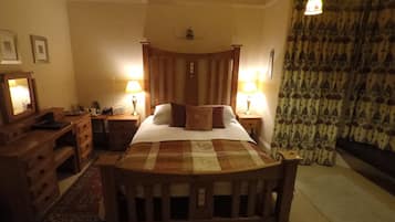Un dormitorio tradicional con una cama de madera con dosel, dos mesitas de noche con lámparas, un aparador y una cortina estampada.