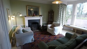 A living room with a fireplace, two armchairs, a sofa, a patterned rug, and a large window with curtains. - Cormiston Farm (Biggar)