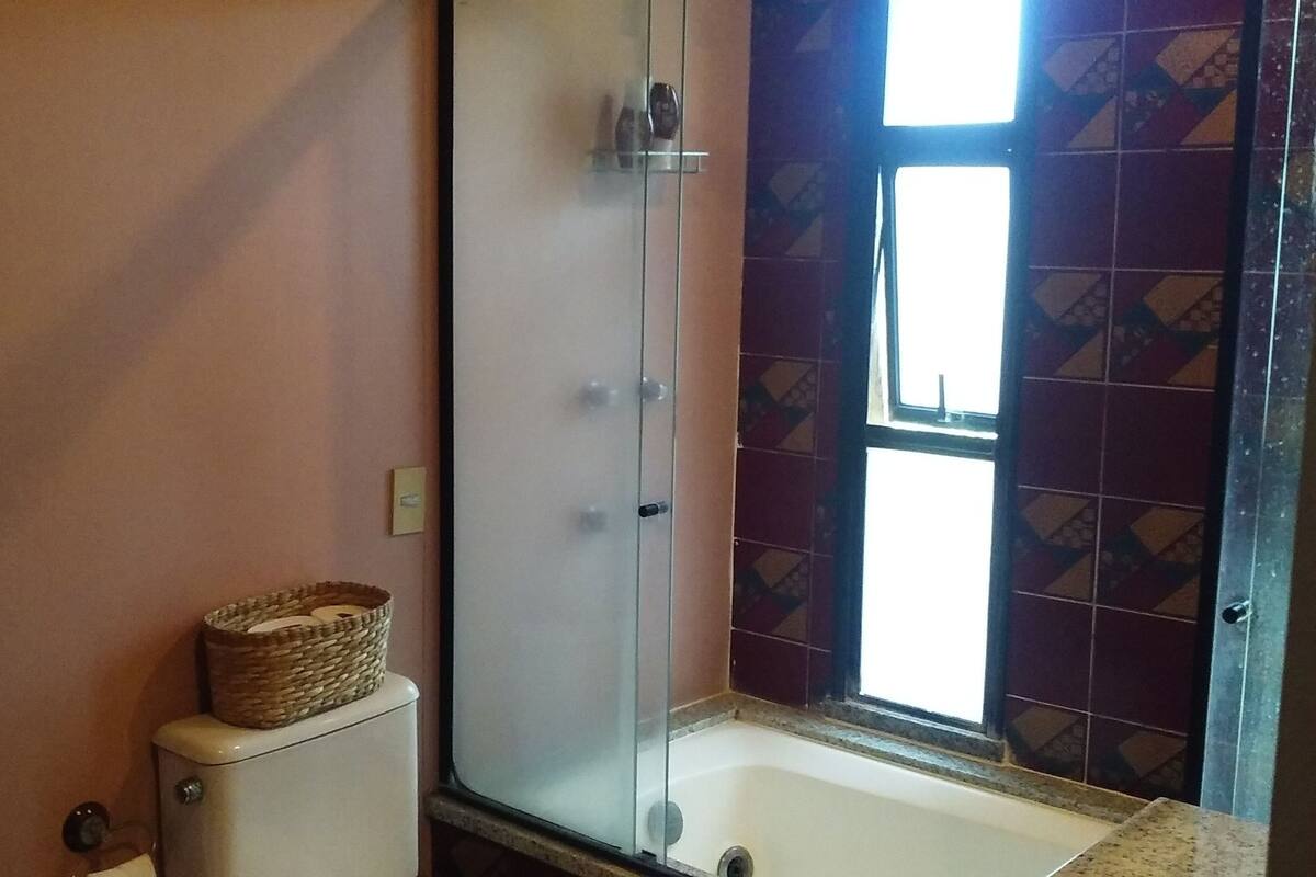 Een badkamer met een douchecabine van glas, een wit bad en een betegelde muur met een geometrisch patroon.