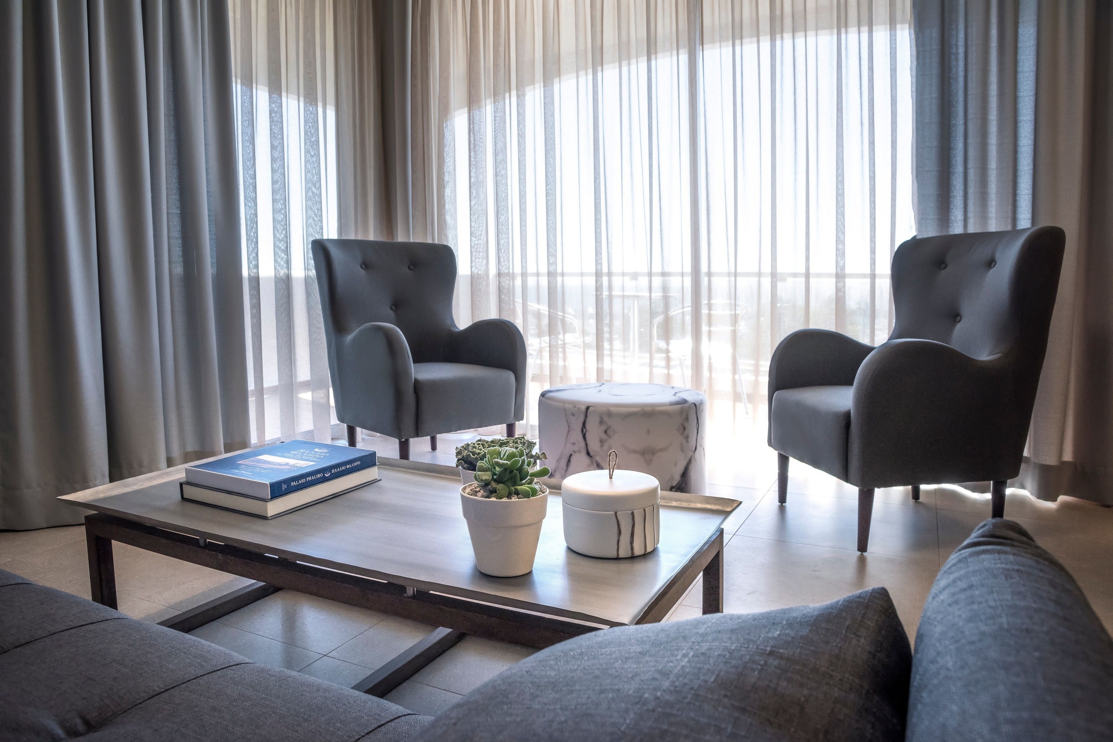 A modern living room with two grey armchairs, a marble coffee table, a book, and a potted plant.