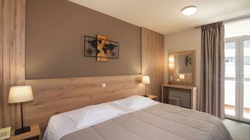 Ein Hotelzimmer mit einem großen Bett, einem Holzkopfstück, zwei Nachttischlampen, einem kleinen Schreibtisch mit Spiegel und einem Wandbild einer Weltkarte.