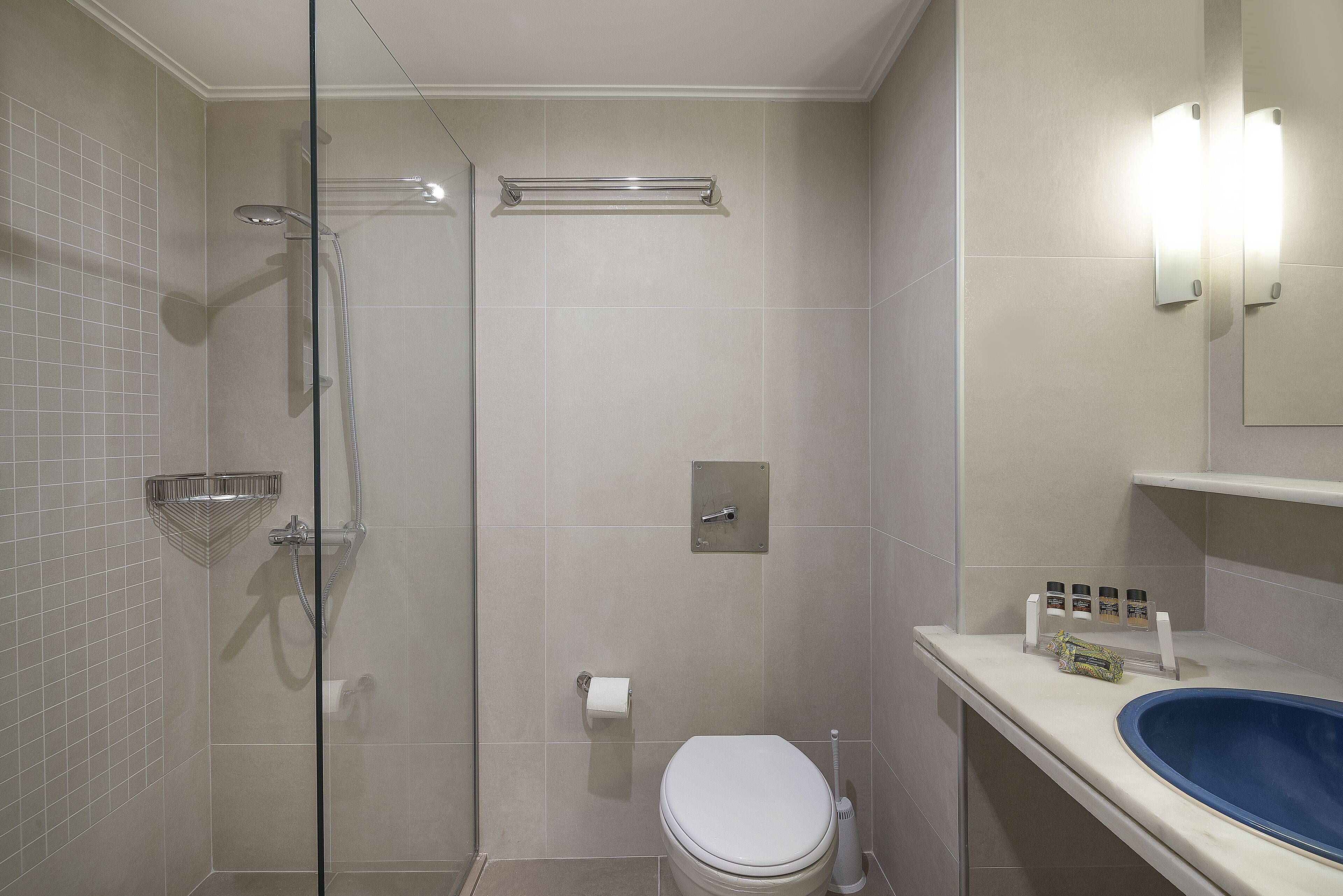 Un baño con cabina de ducha de vidrio, inodoro, lavabo con lavamanos azul y espejo con luces empotradas.