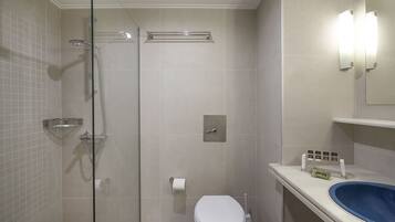 Un baño con cabina de ducha de vidrio, inodoro, lavabo con lavamanos azul y espejo con luces empotradas.
