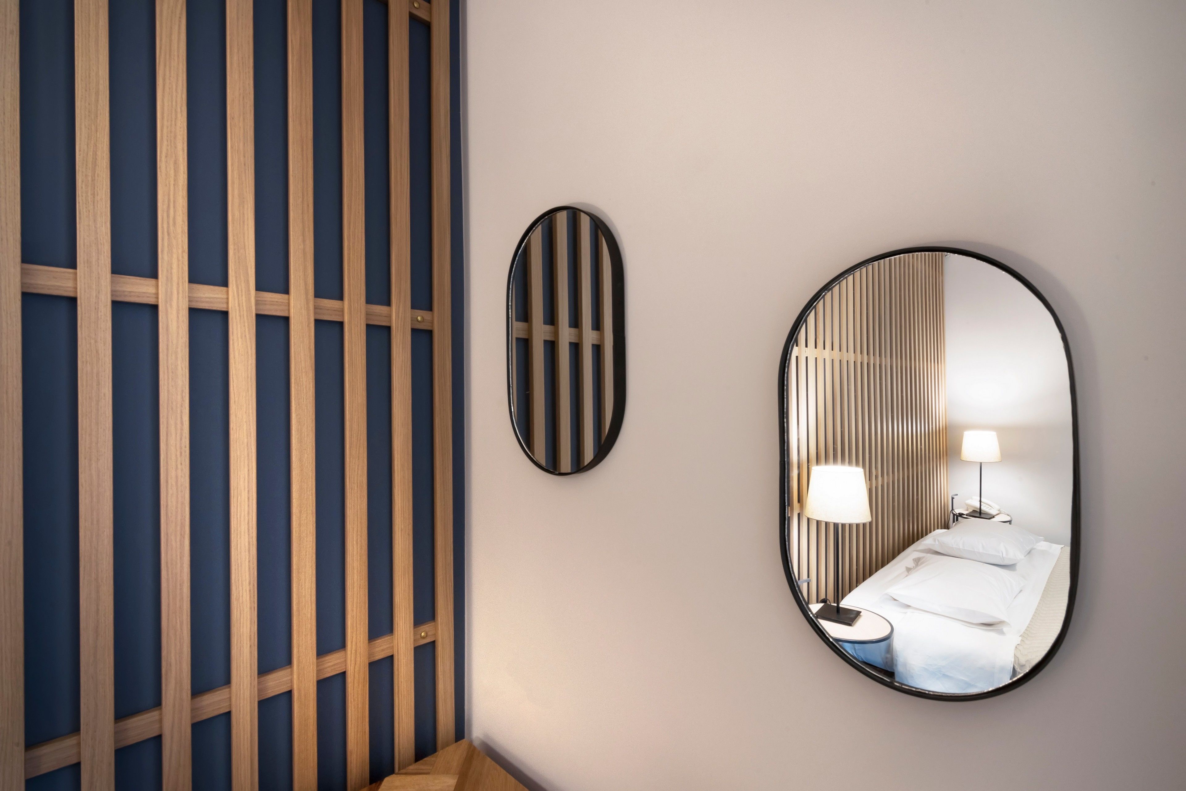 A hotel room with a bed, bedside lamps, and a mirror reflecting the room.