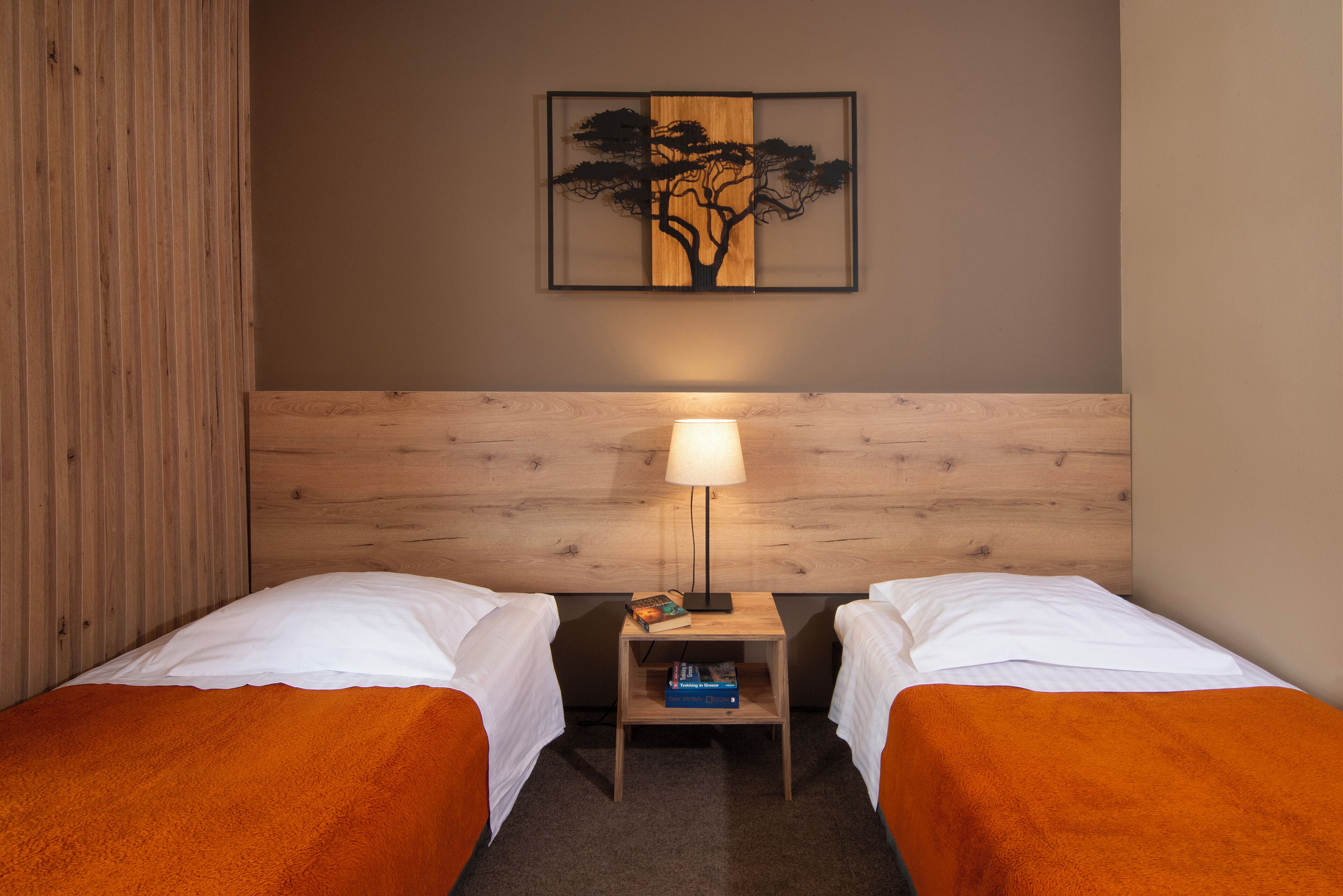 A hotel room with two beds, a nightstand with a lamp, a framed artwork on the wall, and a wooden headboard.