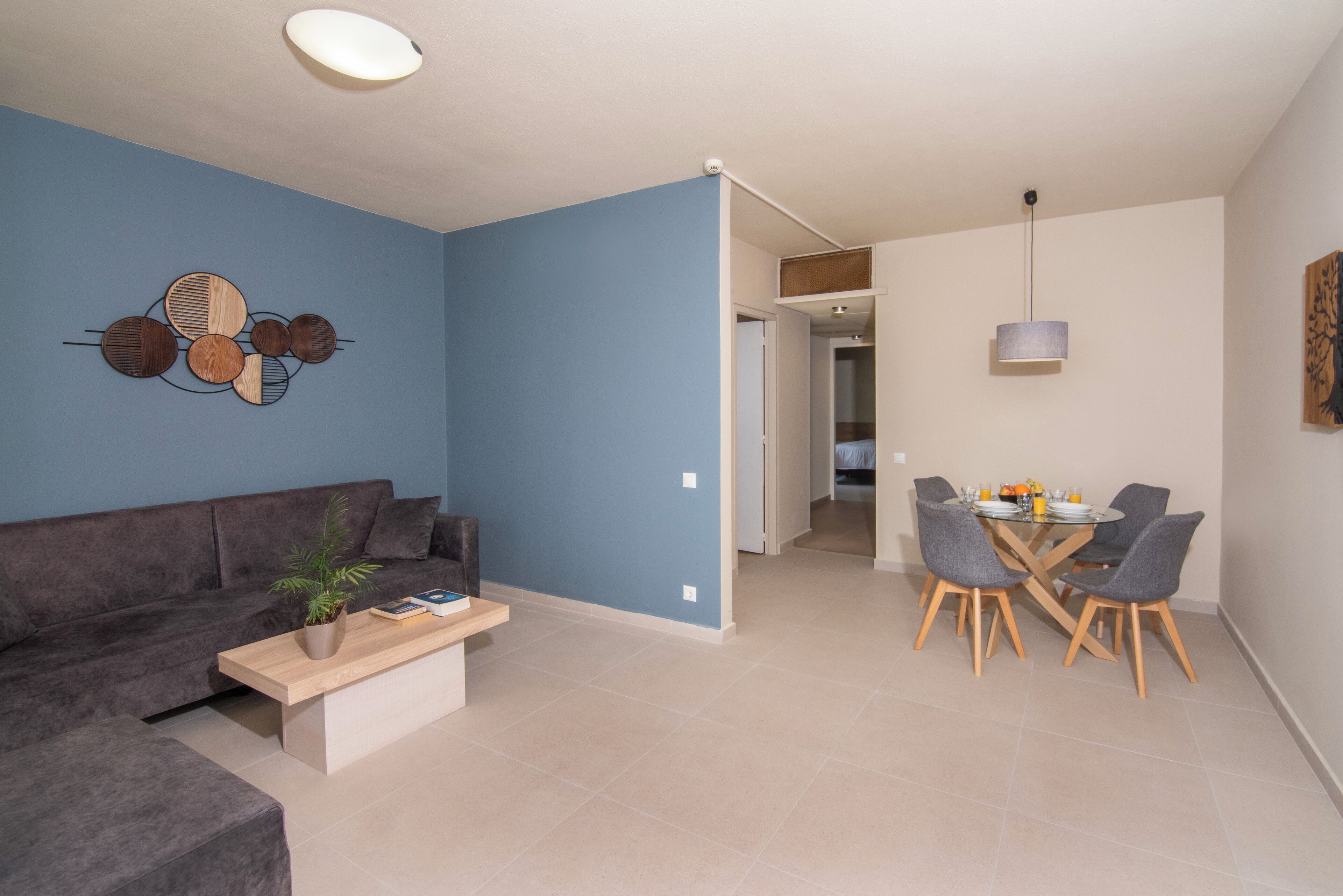 Uma sala de estar moderna com um sofá cinzento, uma mesa de centro de madeira e uma área de jantar com uma mesa e cadeiras.