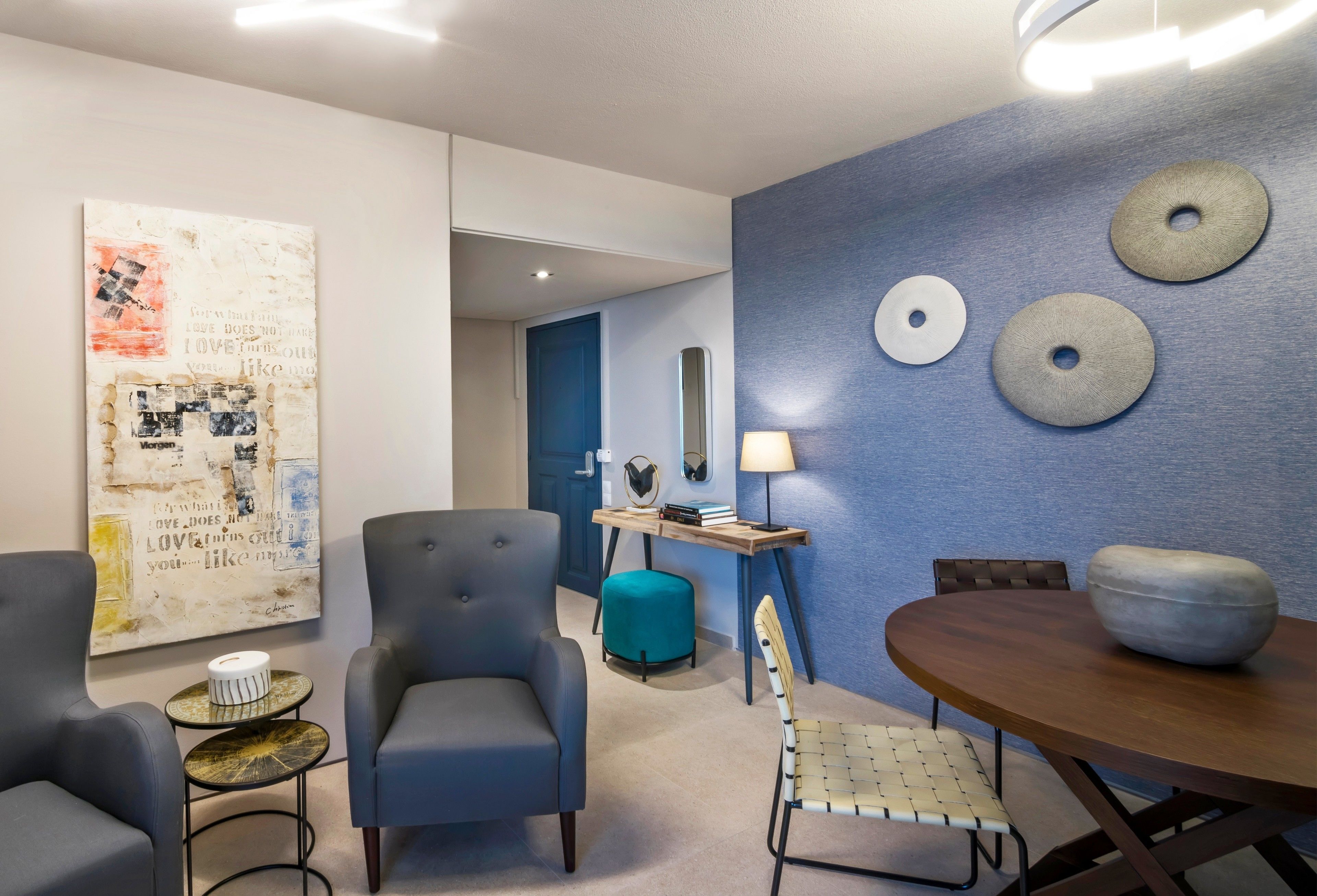 A modern living room with a blue accent wall, a large abstract painting, and a round table with chairs.