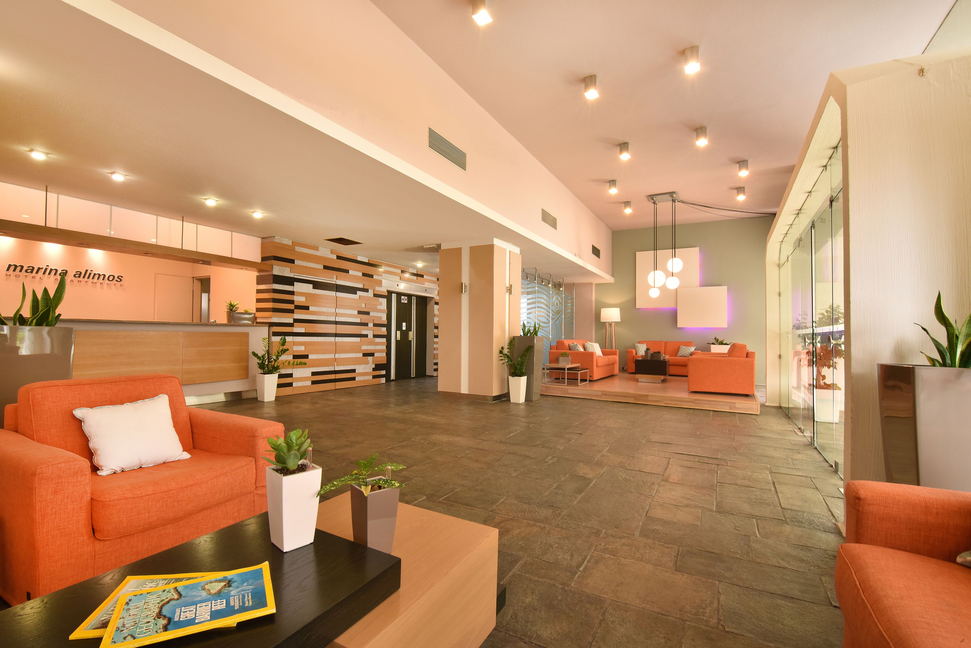 A modern hotel lobby with orange seating, a reception desk, and a large mirror.