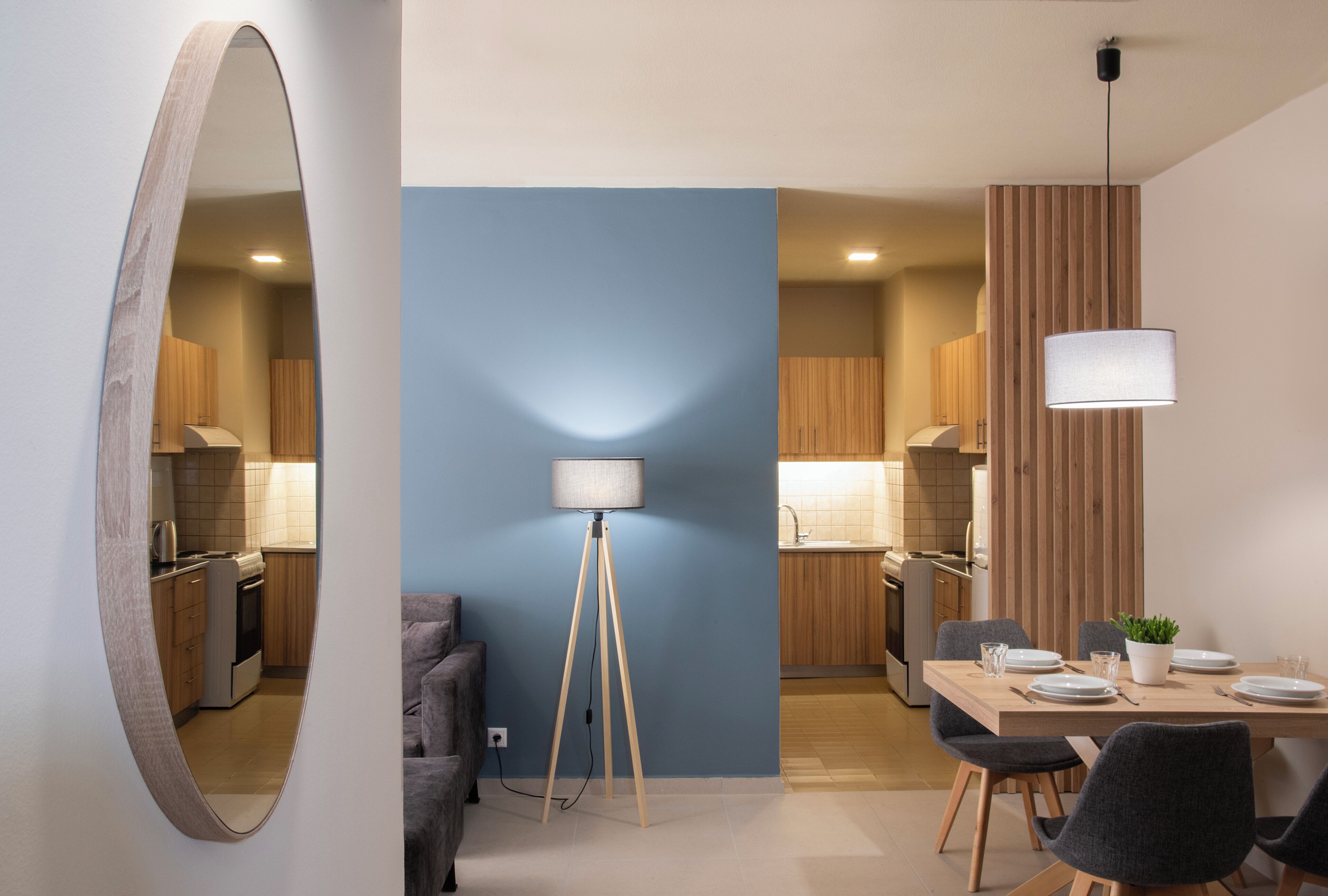 Una cocina moderna con armarios de madera, un comedor con una mesa preparada para cuatro personas, y una lámpara de pie.