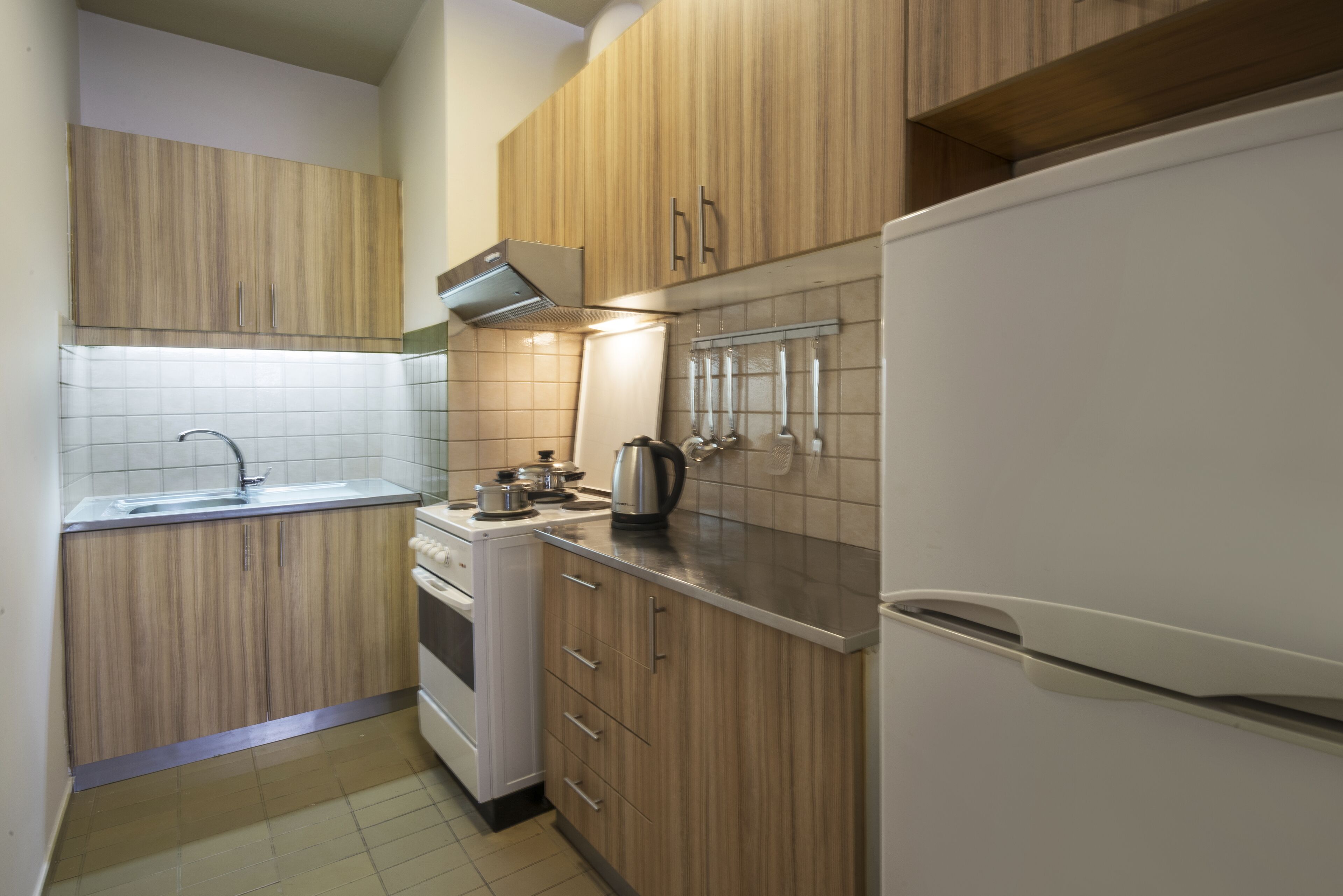 A compact kitchen with wooden cabinets, a stainless steel sink, and a white refrigerator.