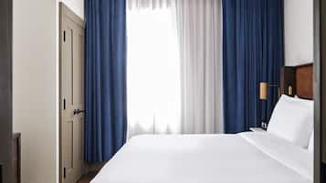 Una habitación de hotel con una cama grande, una mesita de noche, una lámpara y una ventana con cortinas.