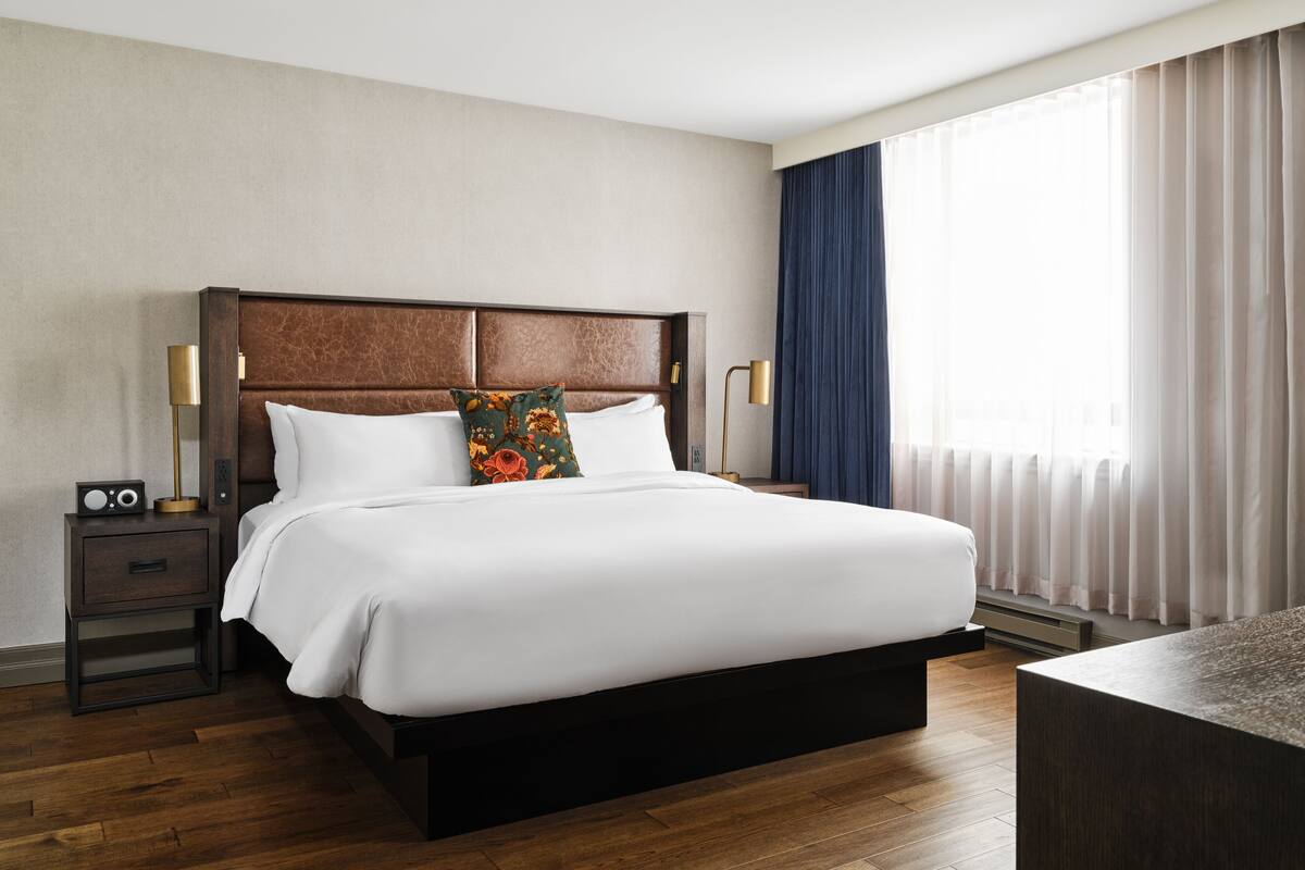 A modern hotel room with a large bed, wooden headboard, and a nightstand with a radio.