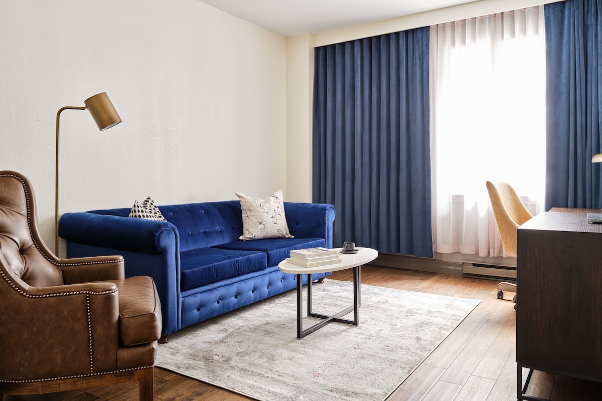 A modern living room with a blue sofa, a brown leather armchair, a round coffee table, and a floor lamp.