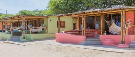 Una hilera de cabañas frente a la playa, con mobiliario exterior y hamacas.