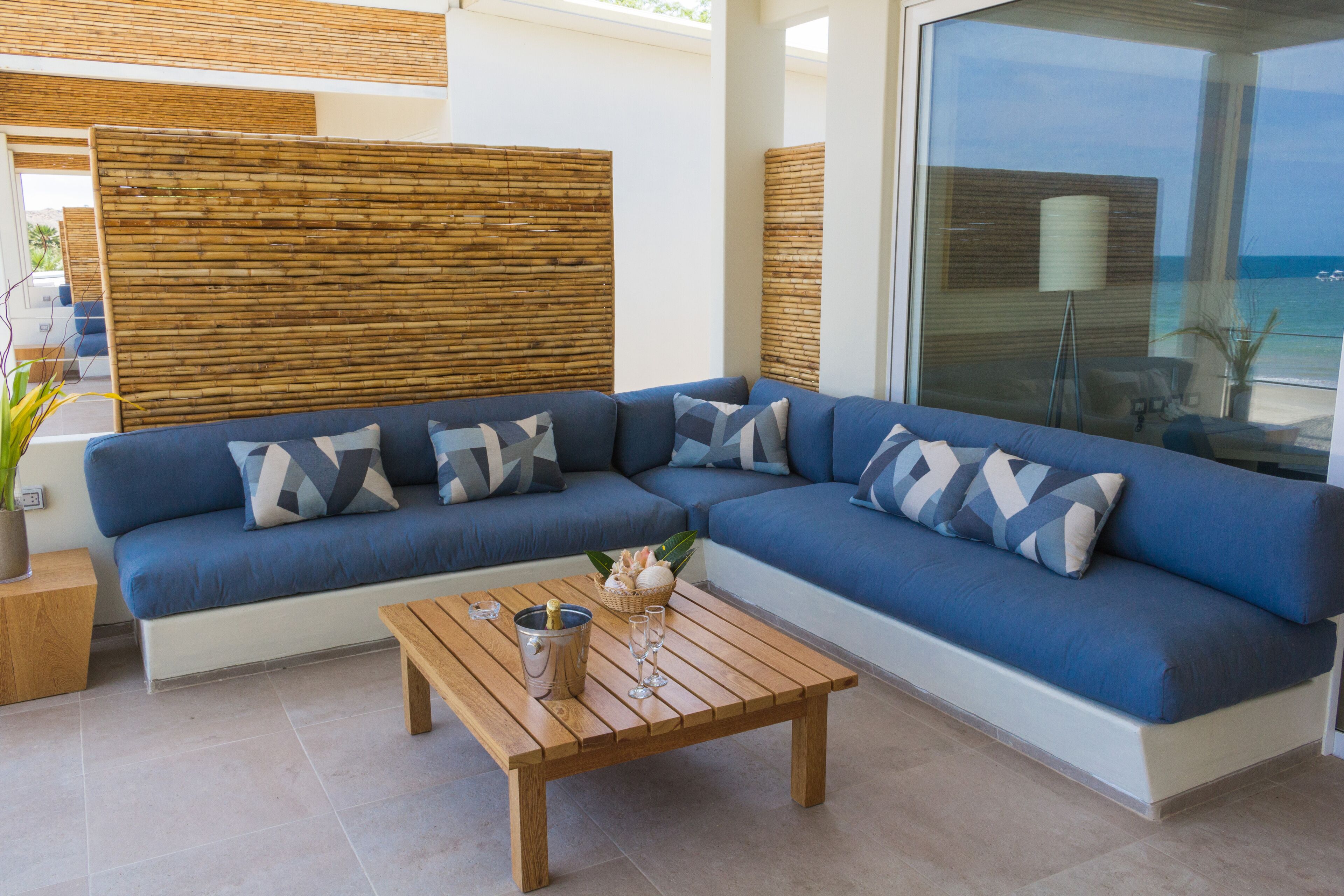 Un espacio exterior moderno con zona de estar, un sofá azul, una mesa de centro de madera y vistas al océano.