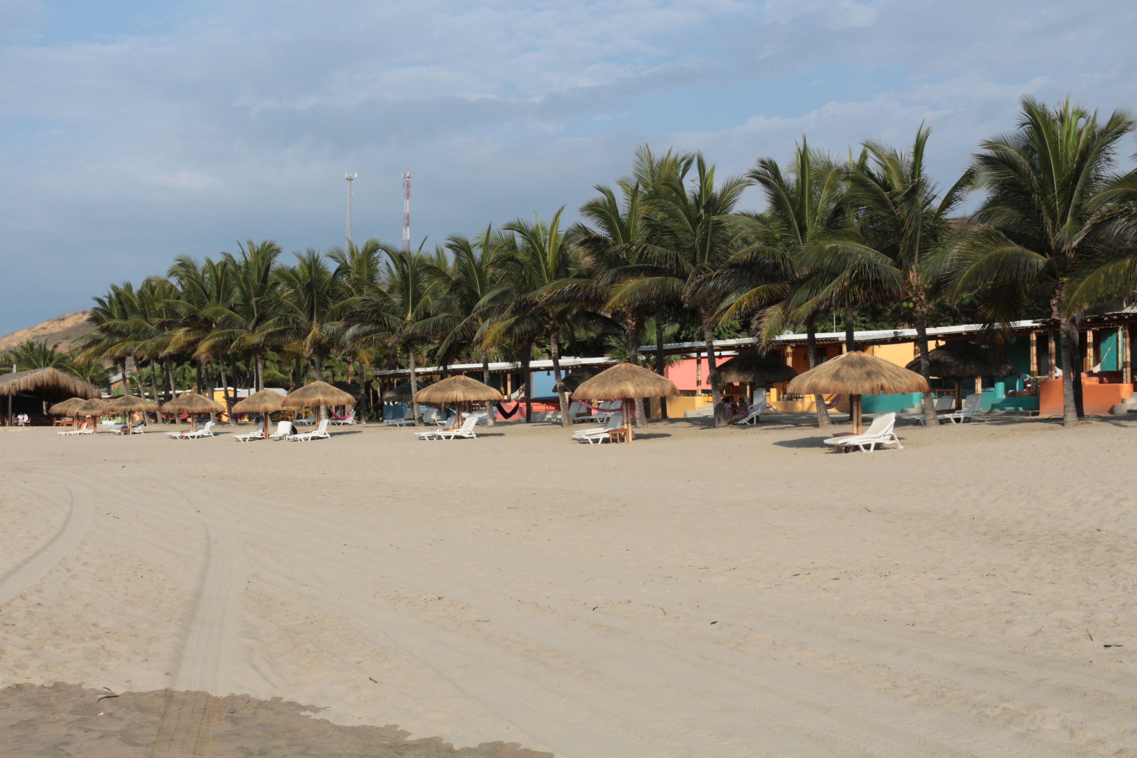 A beach with thatched-roof huts and white lounge chairs.