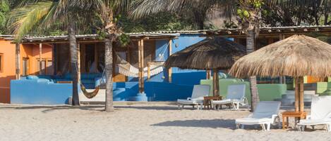 A beachside resort with thatched umbrellas, lounge chairs, and a hammock.