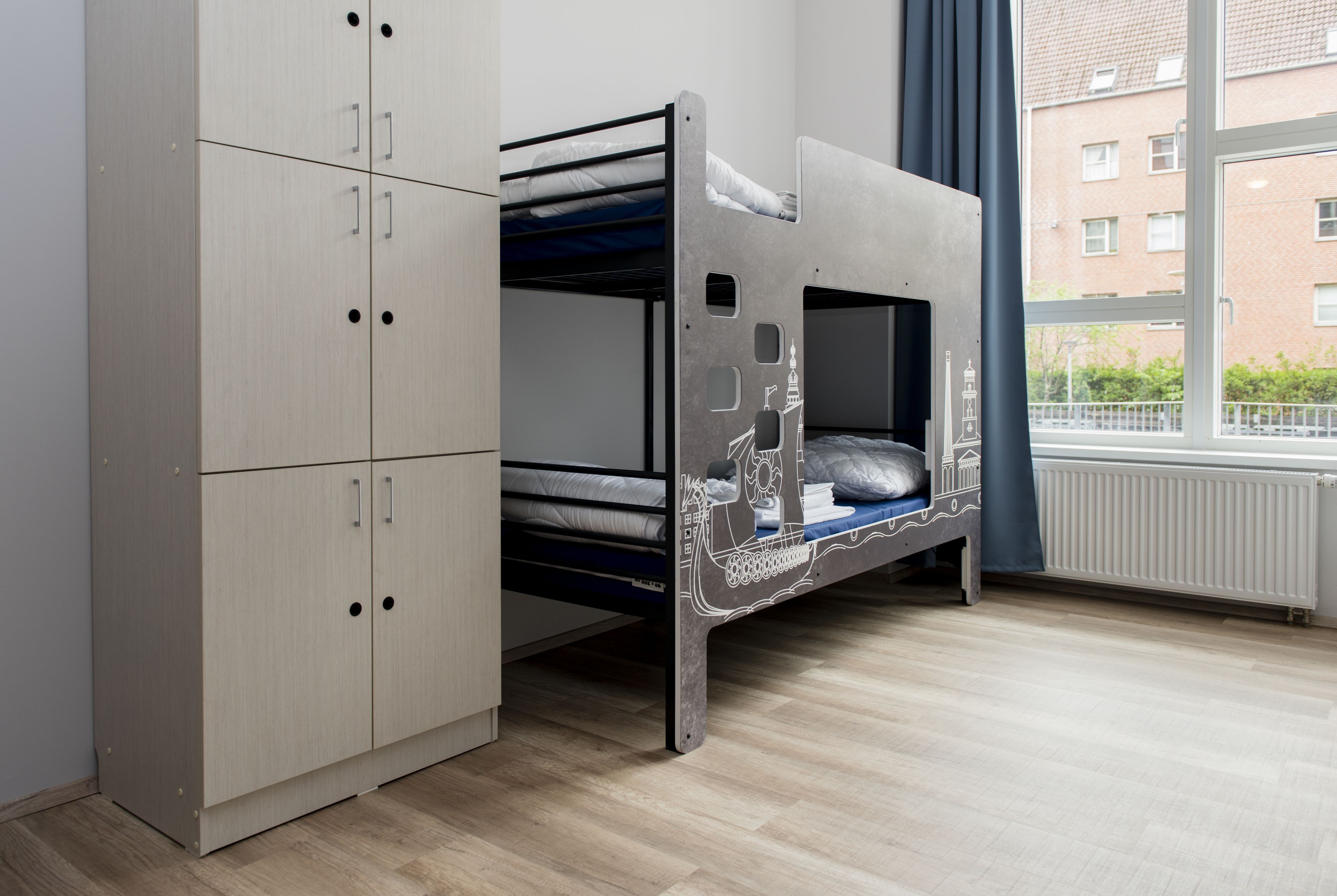 Uma cama beliche com design decorativo, um guarda-roupa com vários compartimentos e uma janela com vista para edifícios.