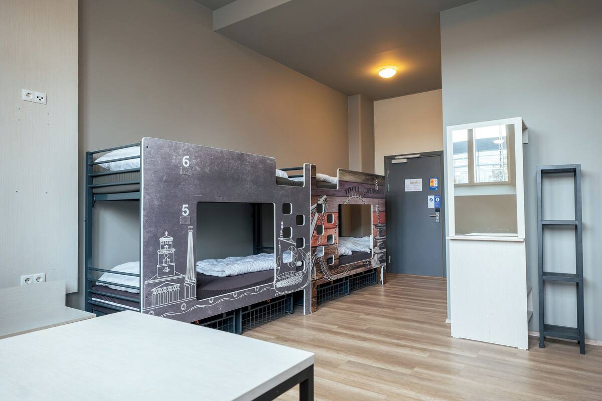A dormitory room with bunk beds, a desk, a window, and a door.