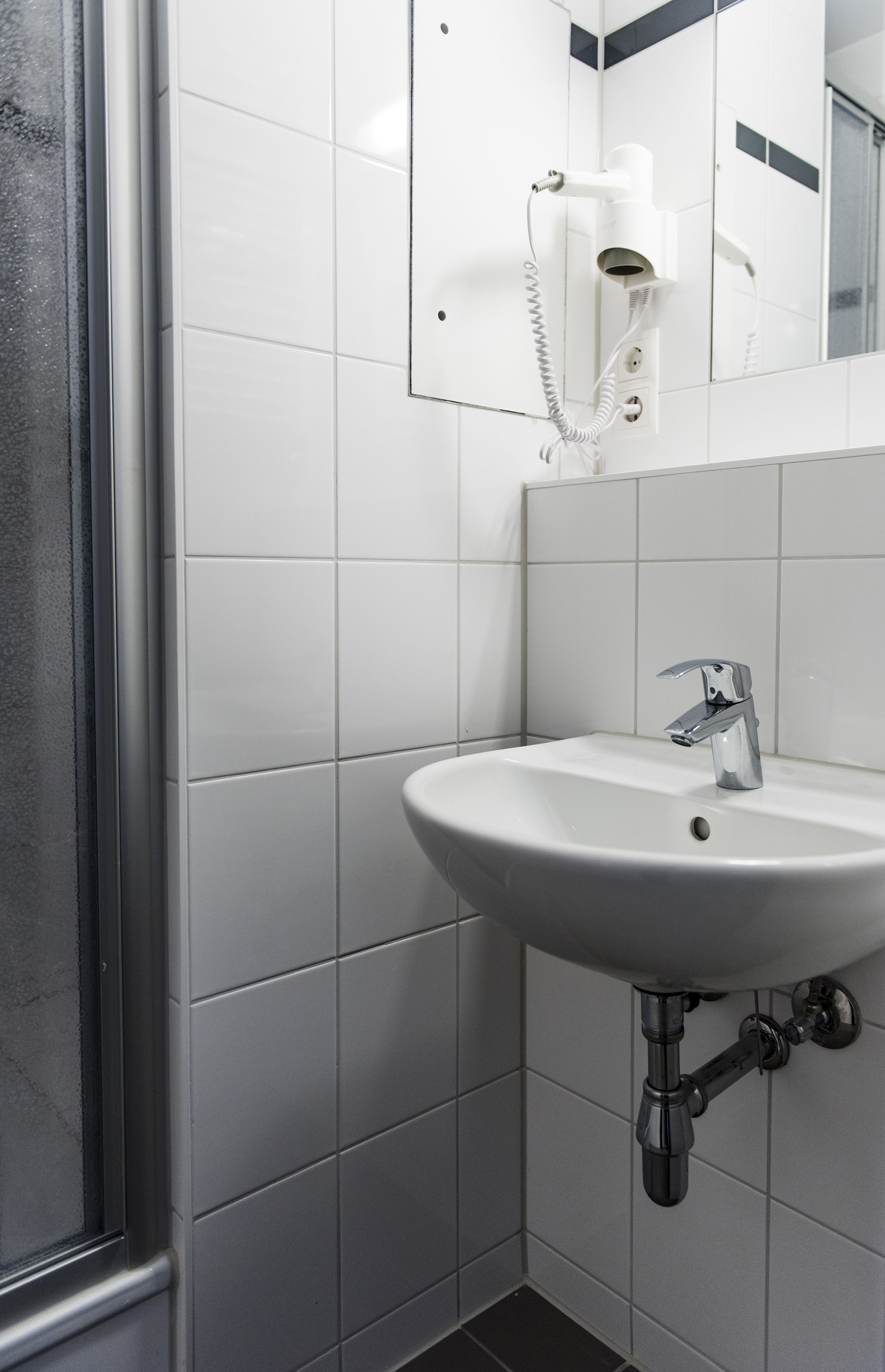 A bathroom with a white sink, chrome faucet, and a hairdryer mounted on the wall.