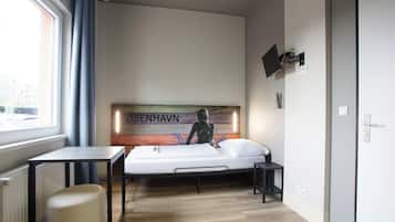 A bedroom with a bed, a table, a chair, a TV mounted on the wall, and a window with curtains.