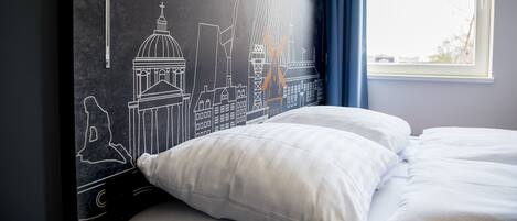 Habitación de hotel con cama, ropa de cama blanca y un mural que representa puntos emblemáticos de Copenhague.