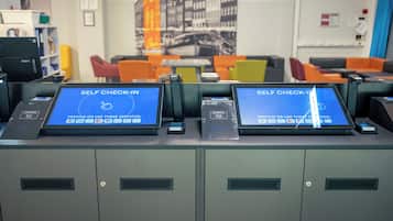 Self-check-in kiosks with a digital interface, a bookshelf, and colorful seating in the background.