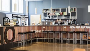 Una zona de bar con taburetes, una barra con un menú y estantes llenos de botellas y vasos.