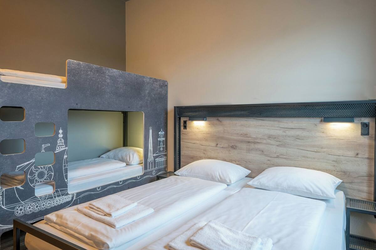A hotel room with bunk beds, a wooden headboard, and a wall with nautical illustrations.