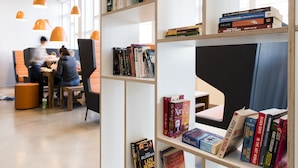 Una biblioteca moderna con estanterías, zona de estar y lámparas colgantes naranjas.