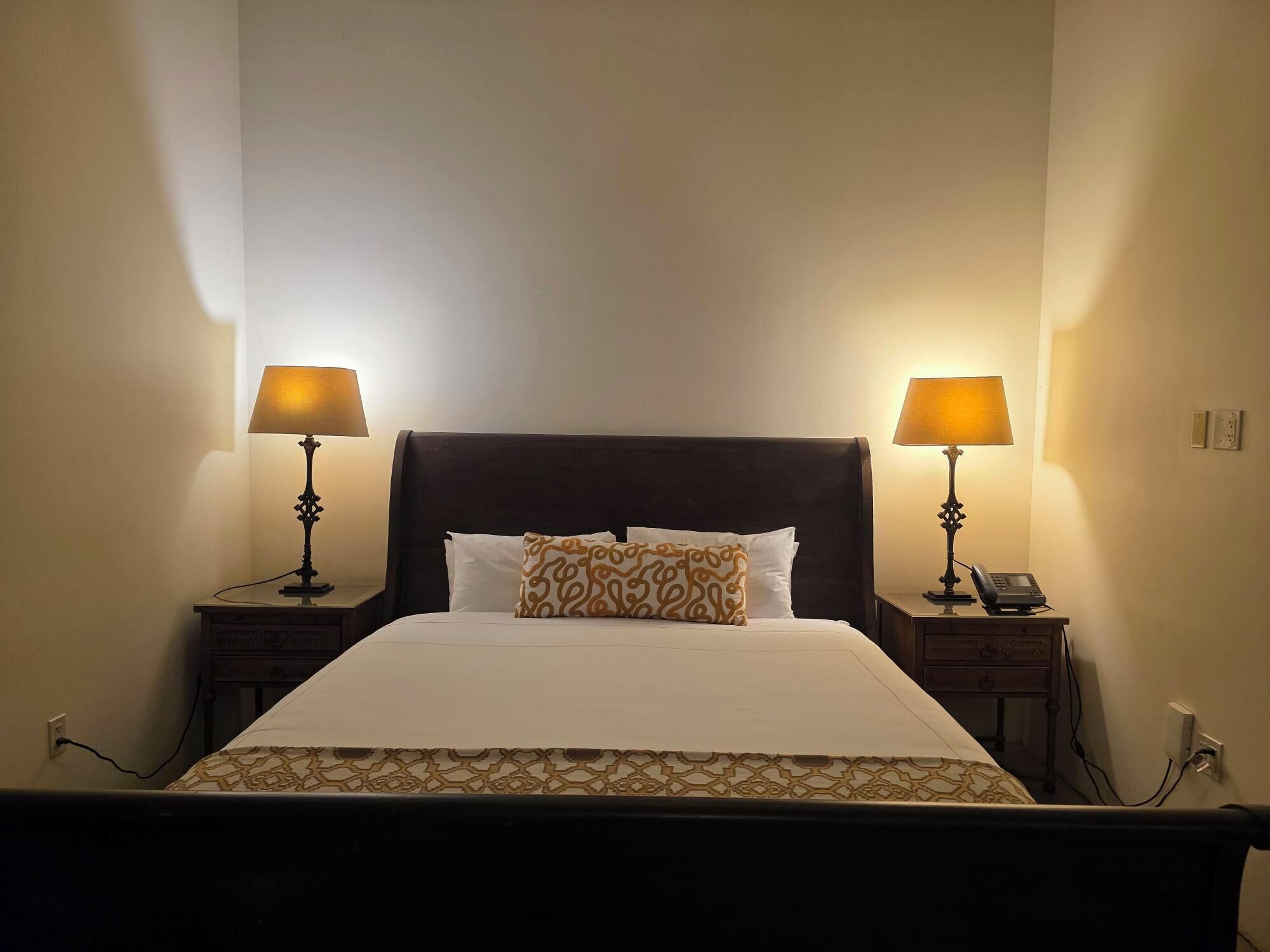 A neatly made bed with a patterned bedspread, two bedside lamps, and a telephone on the nightstand.