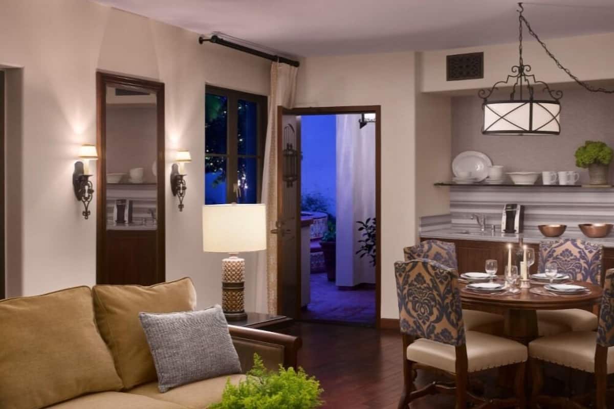 Un salon avec un canapé, une table basse agrémentée d’une plante, un coin repas avec une table et des chaises, et une cuisine en arrière-plan.