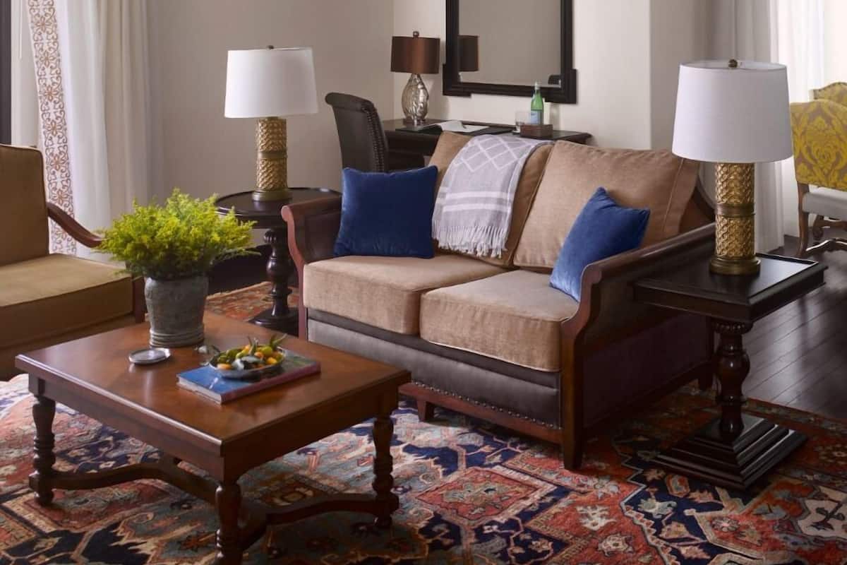 Un salon avec un canapé beige, deux lampes, une table basse et un tapis à motifs.