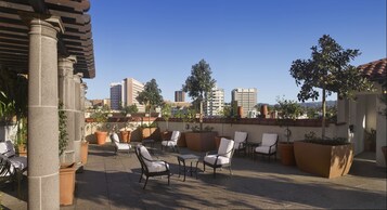 Terraza en la azotea con mobiliario exterior y plantas en macetas, con vistas a un paisaje urbano de edificios altos.