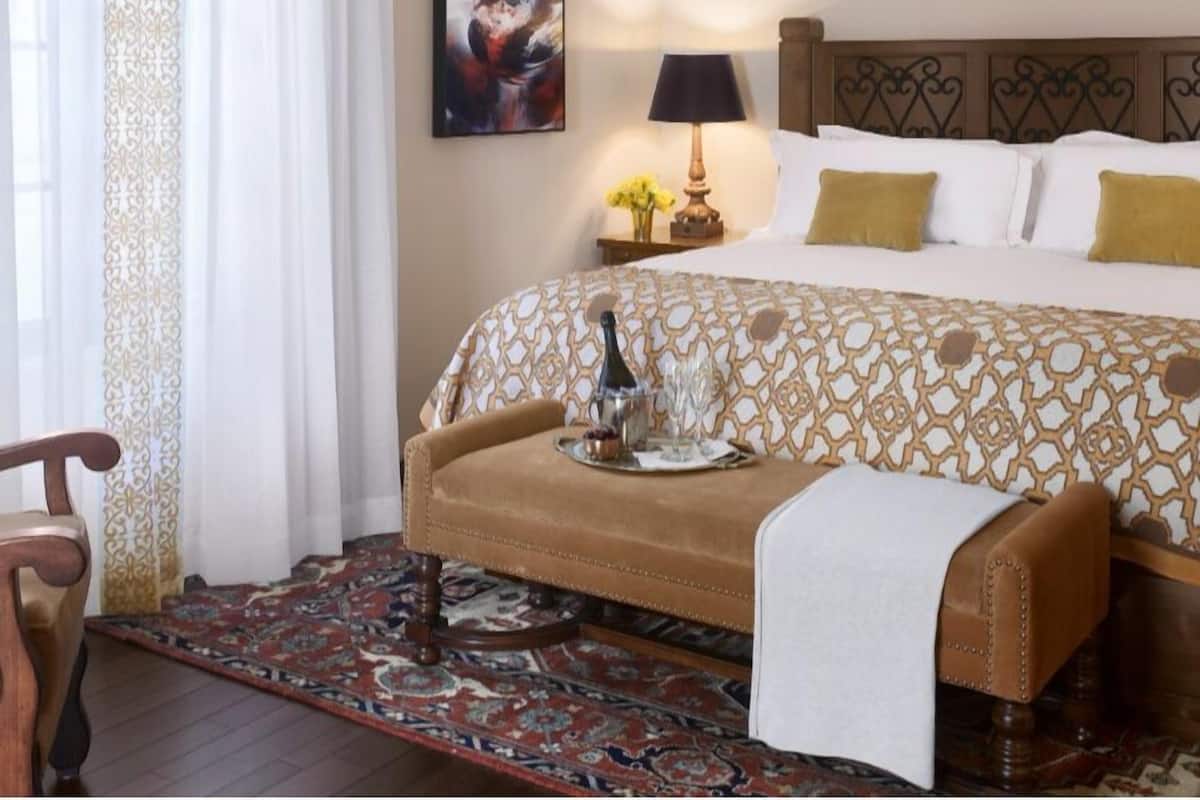 Une chambre d’hôtel avec un lit, une table de chevet avec une lampe, un tableau au mur et un canapé sur lequel se trouve un plateau avec divers objets.