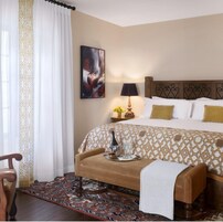 Una camera d'albergo con un letto, un comodino con una lampada, un quadro appeso al muro e un divano con un vassoio di oggetti.