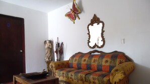 A living room with a sofa, a wooden table, a decorative mirror, and a butterfly decoration on the wall. - Finca Santa Mónica (Xilitla)