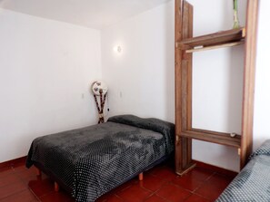 Una habitación pequeña con cama individual, colcha estampada, cabecera de madera y estante en la pared.