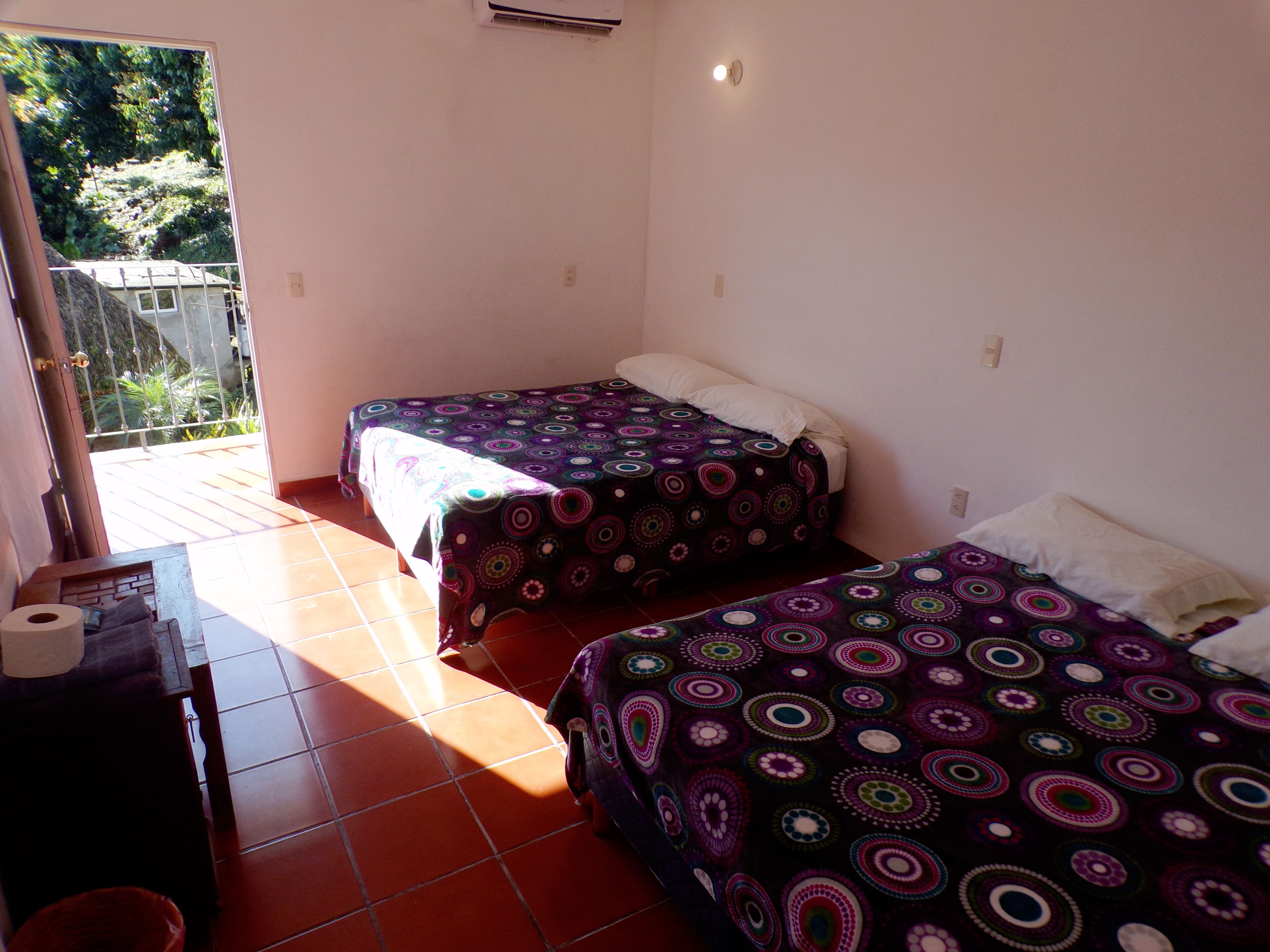 A room with two beds, a small table, and a window overlooking a garden.