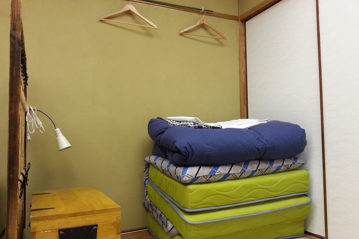 A compact room with a wooden cabinet, a green mattress, and a white lamp.