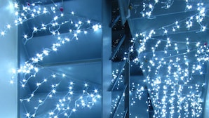 Un escalier décoré de guirlandes lumineuses et surmonté d’un lustre.