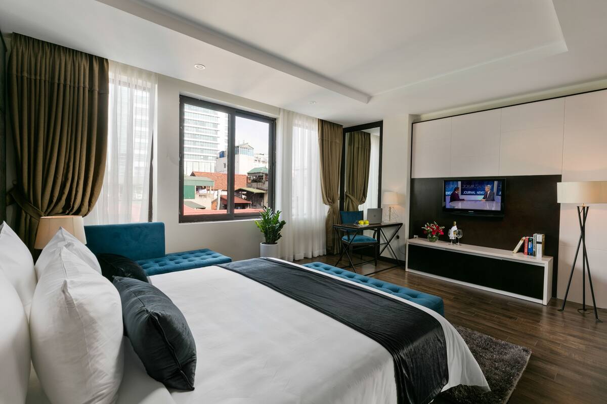 Una habitación de hotel moderna con una cama grande, un escritorio con una silla, un televisor y vistas a la ciudad.