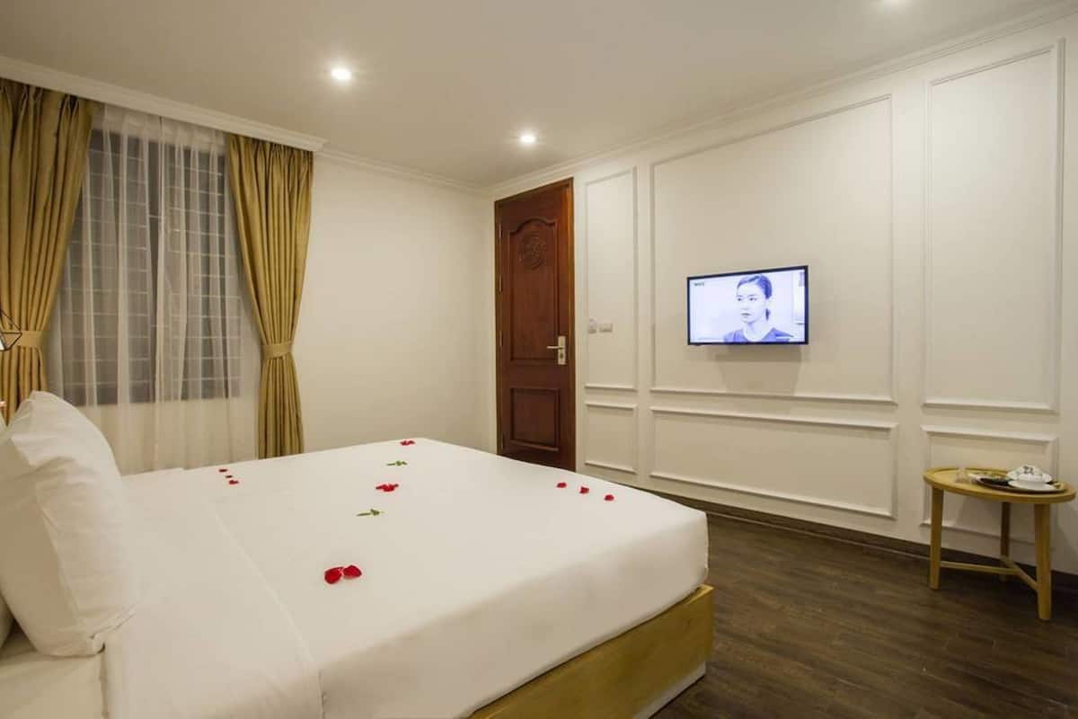 Une chambre d’hôtel avec un lit bien fait, un téléviseur fixé au mur et une petite table avec un plateau.