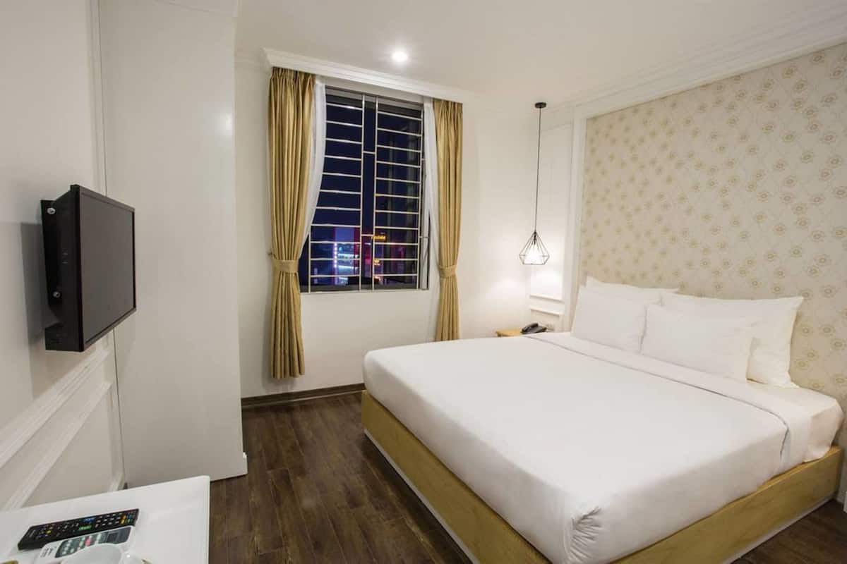Une chambre d’hôtel avec un grand lit, un téléviseur fixé au mur, une fenêtre avec des rideaux et un papier peint à motifs sur le mur.