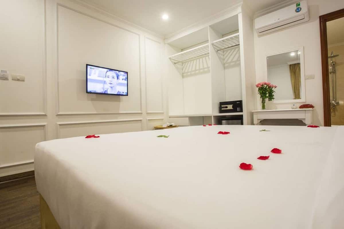 Une chambre d’hôtel avec un grand lit, un téléviseur fixé au mur, un bureau avec un ordinateur et un miroir au-dessus du bureau.