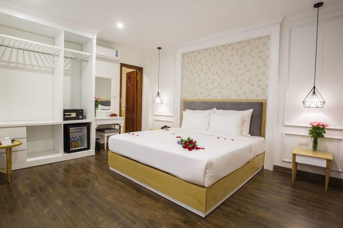 Une chambre d’hôtel comprenant un lit, une armoire, une petite table, une table de chevet et un luminaire suspendu.