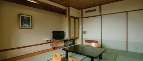 A traditional Japanese room with tatami flooring, a low table, a television, and a painting on the wall.