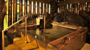 A hot spring area with stone steps leading to a wooden platform, surrounded by wooden beams and rocks. - Kirishima Hotel (Kirishima)