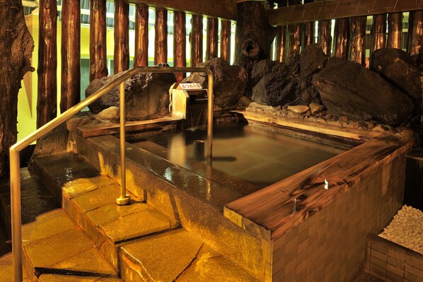 A hot spring area with stone steps leading to a wooden platform, surrounded by wooden beams and rocks.