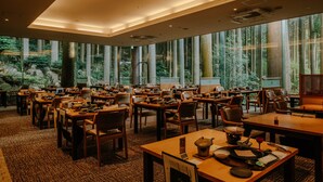 A spacious dining area with multiple tables and chairs, large windows with a forest view, and a modern ceiling design. - Kirishima Hotel (Kirishima)